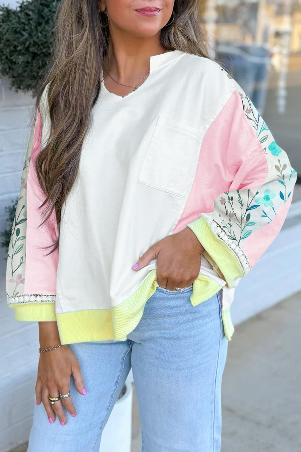 Woman wearing a white blouse with floral sleeves and light blue jeans outdoors.
